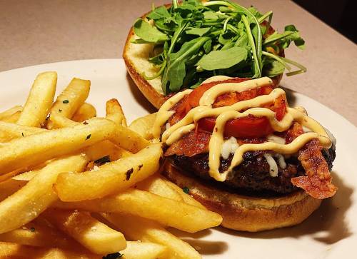 A juicy burger topped with bacon, tomato, and mayo, served with a side of crispy fries and fresh greens.