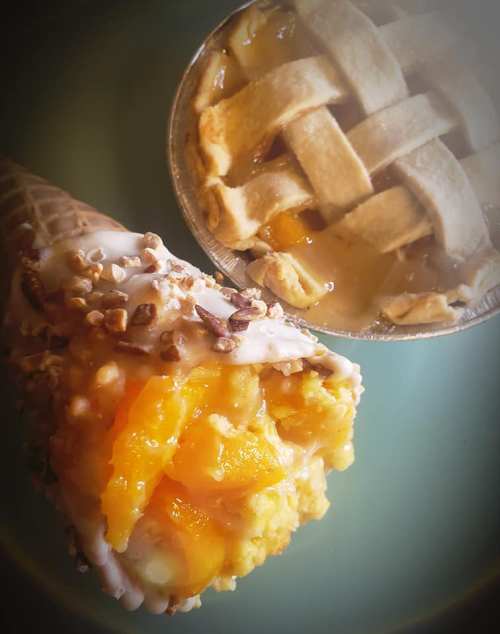 A close-up of a cone filled with mango ice cream and a small pie with a lattice crust and fruit filling.
