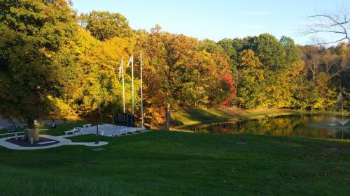 A serene park scene with colorful autumn trees, a pond, and a memorial area with flags.