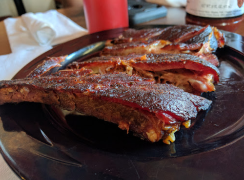 Close-up of a plate with three pieces of smoked ribs, showcasing a crispy exterior and tender meat.