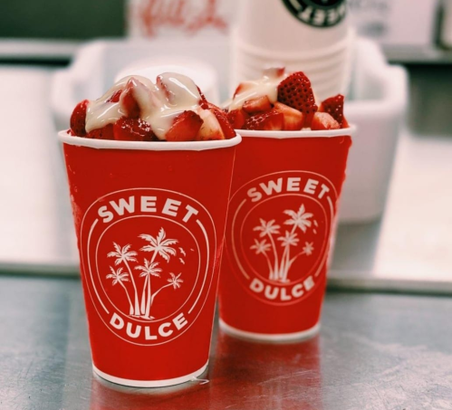 Two red cups filled with strawberries and cream, featuring the logo "Sweet Dulce" with palm trees.