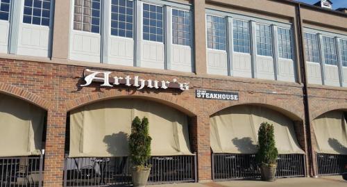 Exterior of Arthur's Steakhouse, featuring a brick facade and large windows, with closed curtains and potted plants.