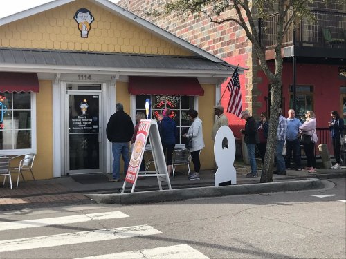 A colorful ice cream shop with a line of people waiting outside, featuring an "Open" sign and American flags.