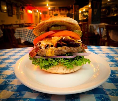 A delicious burger stacked with lettuce, tomato, cheese, bacon, and onion on a plate, set in a cozy restaurant.