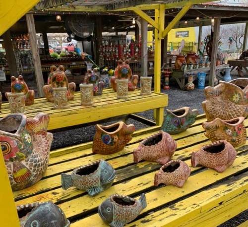 Colorful ceramic fish and frog planters displayed on a bright yellow wooden table at an outdoor market.