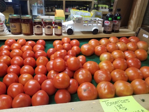 A display of ripe red tomatoes on a green surface, with jars and a small toy truck in the background.