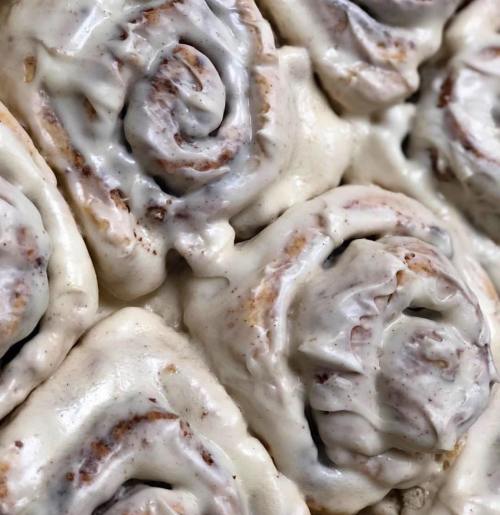Close-up of freshly baked cinnamon rolls topped with creamy icing, showcasing their swirled layers and soft texture.