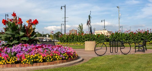 A vibrant flower garden with colorful blooms, bike racks, and benches under a blue sky with scattered clouds.