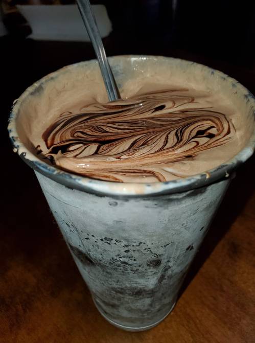 A metal cup filled with swirled chocolate and cream, with a spoon resting inside.