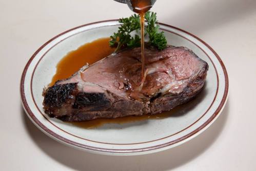 A slice of roast beef on a plate, drizzled with gravy and garnished with parsley.