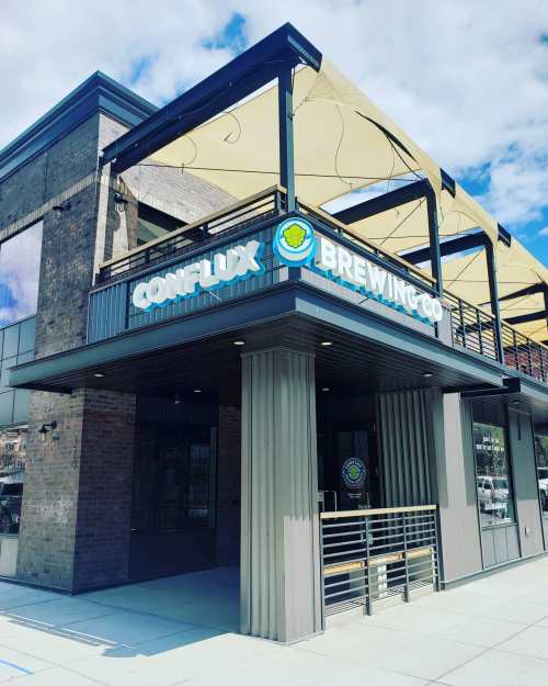 Exterior of Conflux Brewing Co. featuring a modern building with a large sign and outdoor seating area under a canopy.