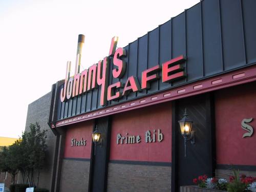 Sign for Johnny's Cafe featuring "Steaks" and "Prime Rib" with decorative lanterns on the building exterior.