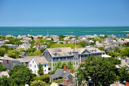 A scenic view of a coastal town with green trees, houses, and a blue ocean under a clear sky.