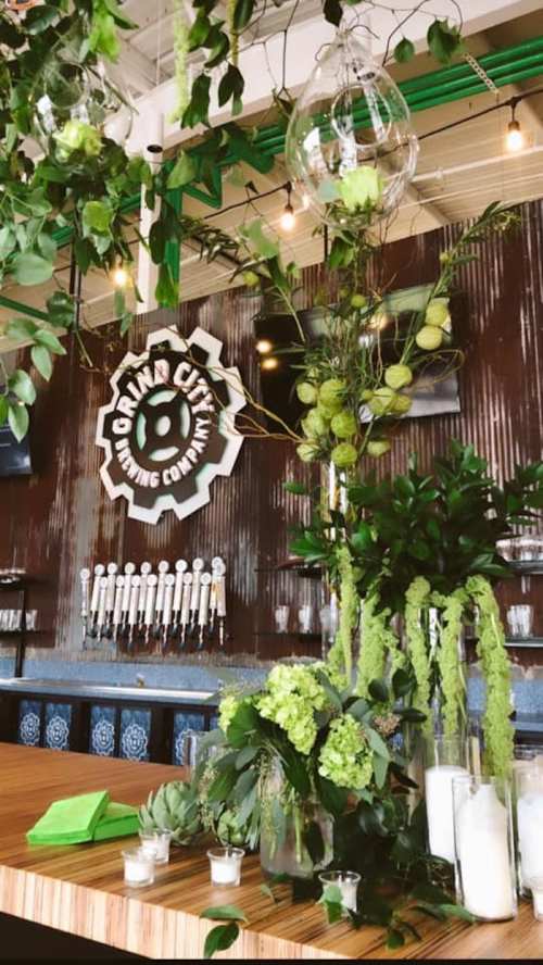 A vibrant bar area with greenery, decorative plants, and a logo, featuring beer taps in the background.