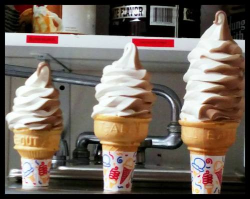 Three soft-serve ice cream cones in waffle cones, two with chocolate and vanilla swirl, one with just vanilla.