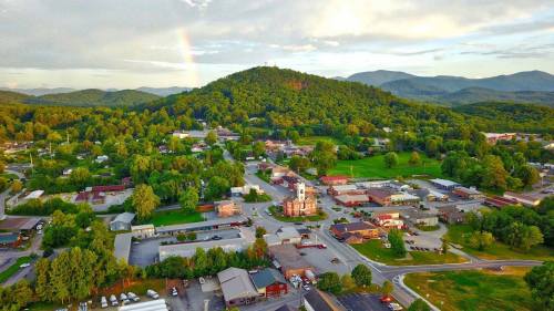 Aerial view of a small town surrounded by green hills, with a rainbow in the sky and a historic building in the foreground.