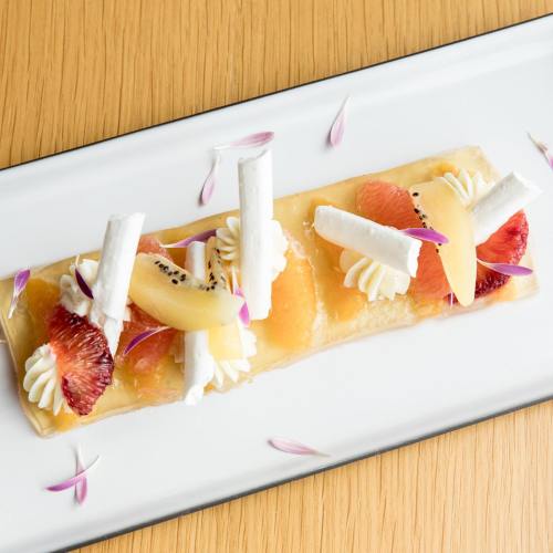 A dessert featuring layered fruit, cream, and meringue on a rectangular plate, garnished with edible flowers.