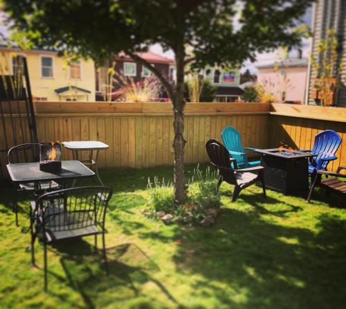 A cozy backyard with green grass, a wooden fence, and various outdoor chairs and tables, some with small fires.