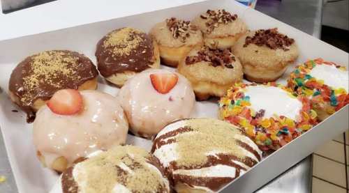 A box of assorted donuts with various toppings, including chocolate, strawberry, and colorful cereal.