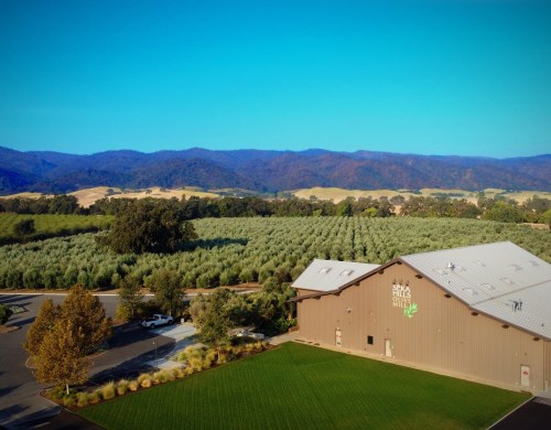 Aerial view of a large building surrounded by lush green fields and rolling hills under a clear blue sky.