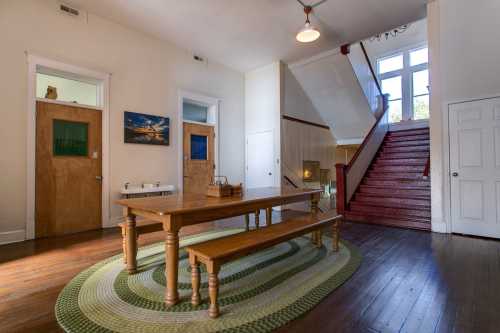 A spacious entryway with a wooden table, benches, and a staircase leading to the upper floor. Natural light fills the room.