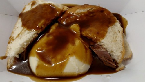A sandwich filled with tender meat and topped with gravy, served with a side of mashed potatoes.