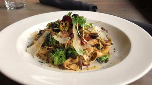 A plate of pasta with broccoli, herbs, and a flower garnish, served on a white dish.