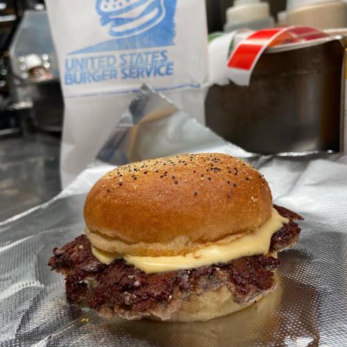 A close-up of a burger with a toasted bun, melted cheese, and a beef patty, set against a blurred background.