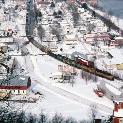 Aerial view of a snowy town with a train passing through, surrounded by houses and industrial buildings.