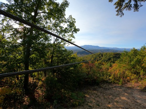 A scenic view of mountains and trees, with zip line cables stretching across the foreground.