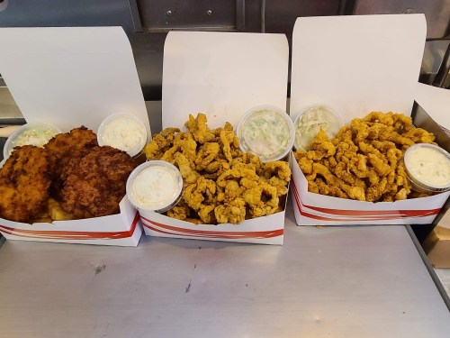 Three boxes of fried food: two with fish fillets and one with fried chicken pieces, each accompanied by dipping sauces.