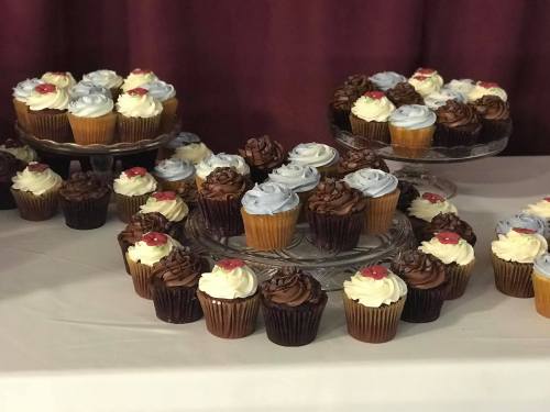 A display of assorted cupcakes in various flavors, topped with blue, white, and chocolate frosting, on glass stands.