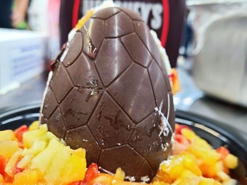A chocolate egg on a bed of colorful diced fruit, with a drizzle of sauce in the background.