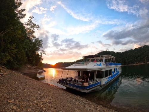A houseboat docked by the shore at sunset, surrounded by trees and calm water.