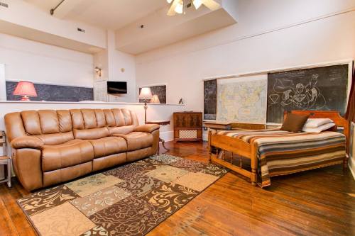 Cozy room with a brown leather sofa, a bed, a rug, and chalkboard walls, featuring warm lighting and wooden floors.
