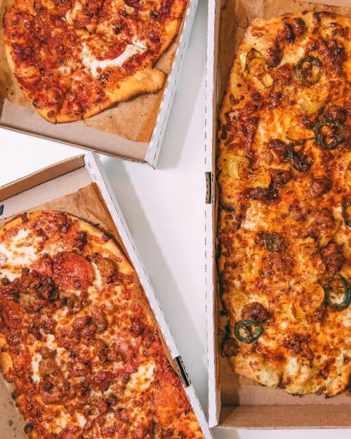 Three pizza boxes open, showcasing different types of pizza with various toppings, including pepperoni and jalapeños.