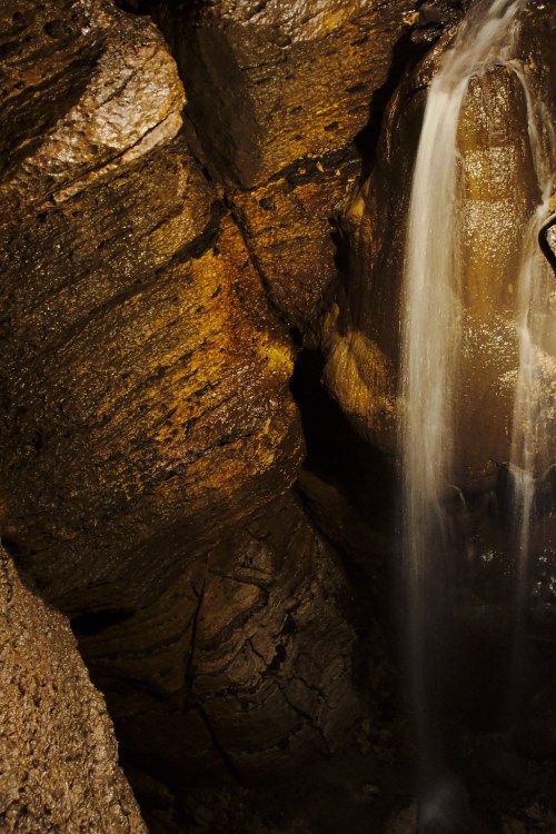 A waterfall cascading over textured rock formations in a dimly lit cave.