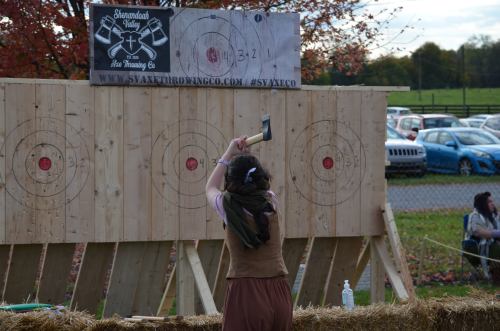 A person prepares to throw an axe at a target board during an outdoor axe-throwing event.