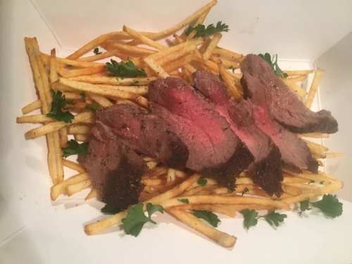 Sliced steak on a bed of crispy fries, garnished with fresh parsley.
