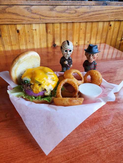 A cheeseburger with lettuce and onion, onion rings, and dipping sauce, alongside two figurines of horror movie characters.