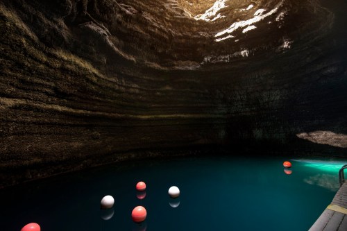A serene underground pool with colorful buoys, surrounded by textured rock walls and illuminated by natural light.