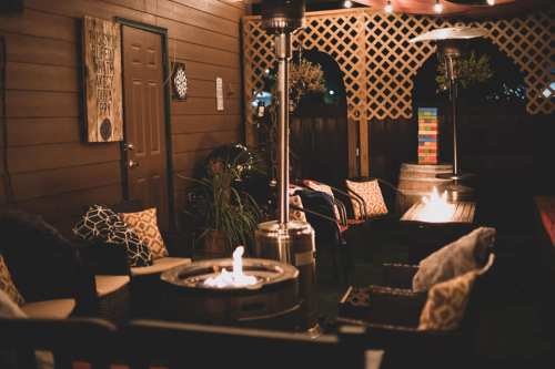 Cozy outdoor seating area with a fire pit, patio heaters, and decorative lighting under a wooden pergola.