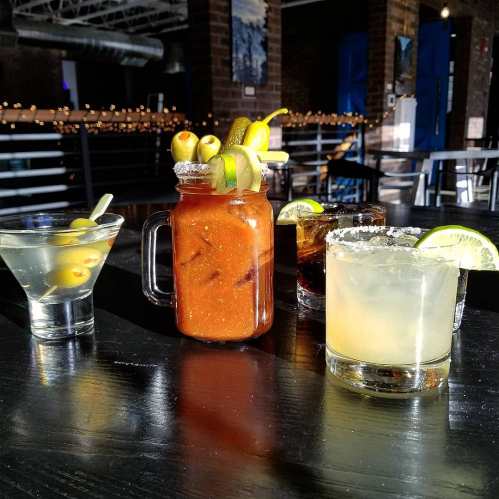 A variety of cocktails on a table: a martini, a Bloody Mary, a dark drink, and a margarita, all garnished with fruit.