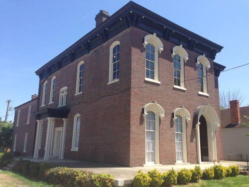 Historic brick building with arched windows and a decorative roof, set against a clear blue sky.