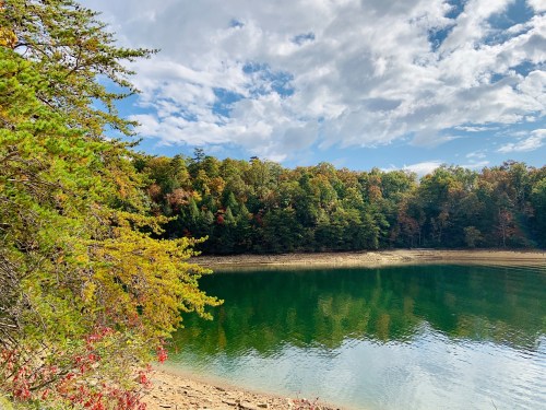 A serene lake surrounded by colorful autumn trees under a partly cloudy sky.