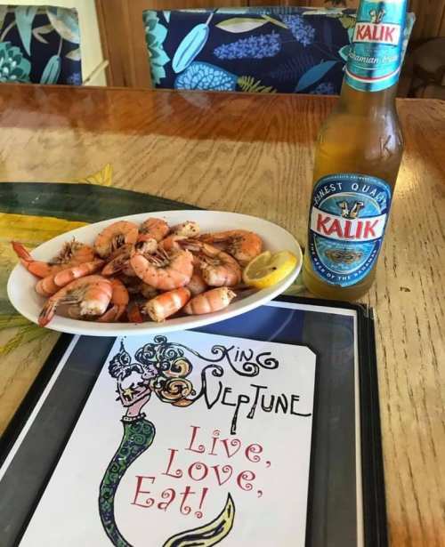 A plate of shrimp with a lemon slice, a Kalik beer, and a menu featuring a mermaid illustration.
