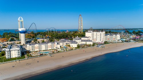 Aerial view of a beachside amusement park with roller coasters, hotels, and a clear blue sky.