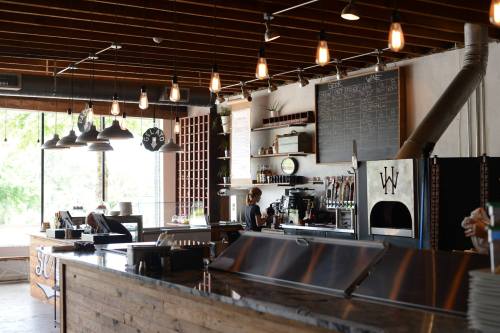 A modern café interior with a wooden counter, coffee machine, and a large chalkboard menu, featuring warm lighting.