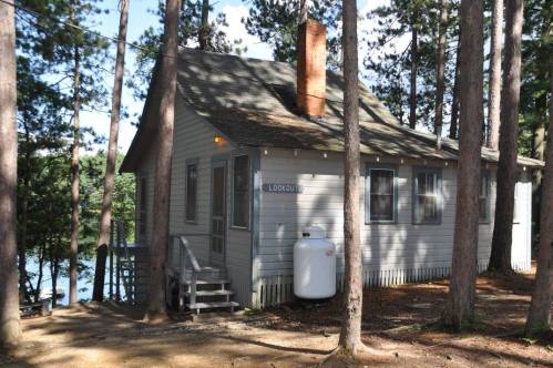 A cozy gray cabin named "Lookout" surrounded by tall pine trees near a lake.