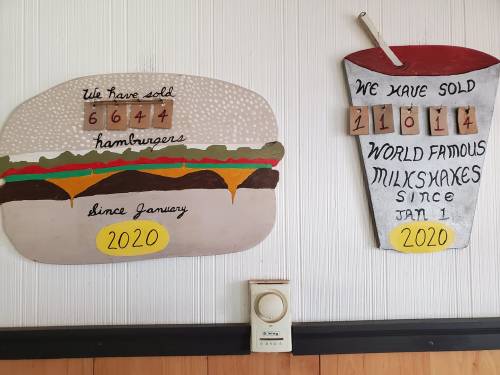 Two signs on a wall: one shows 6,644 hamburgers sold since January 2020, the other 11,014 milkshakes sold since January 1, 2020.